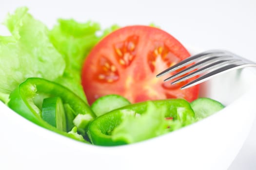 fork,lettuce, tomato, cucumber and pepper in a bowl isolated on white
