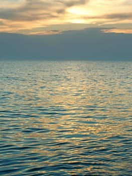 Sea after sunset. Yellow-orange clouds reflected on surface of light sea waves