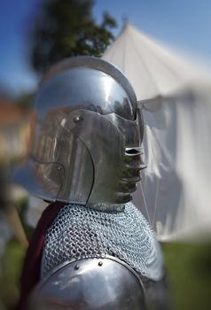 Knight in coat of mail and helmet in front of his tent ready for a fight.