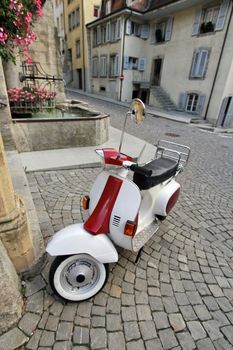 Classical white and red scooter parked in narrow old street of Estavayer-le-lac, Fribourg canton, Switzerland