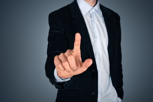 Portrait of pensive handsome businessman touching a blank invisible screen. Touch screen concept image. Isolated on dark gray background. 