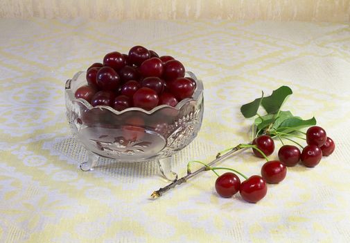 Ripe cherries in a small crystal vase and a branch with cherries.