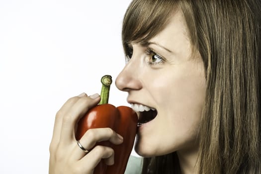 Young beautiful woman biting into a red pepper, isolated on white background