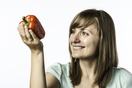 Young woman looks at a red pepper, isolated on white background