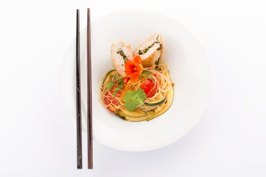 Asian food with piece of stuffed chicken, noodles, zucchini, carrots and tomatoes.