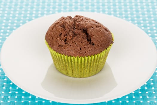 Delicious homemade chocolate muffin on white plate on blue tablemat.