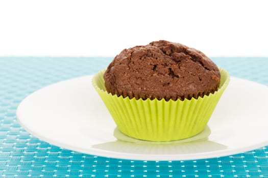 Delicious homemade chocolate muffin on white plate on blue tablemat.