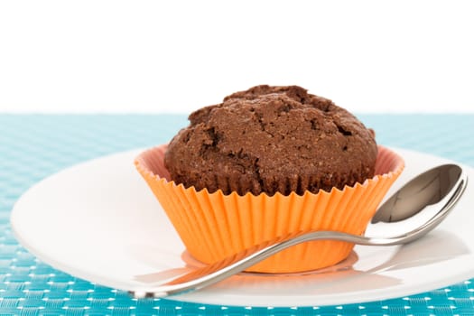 Delicious homemade chocolate muffin on white plate on blue tablemat.