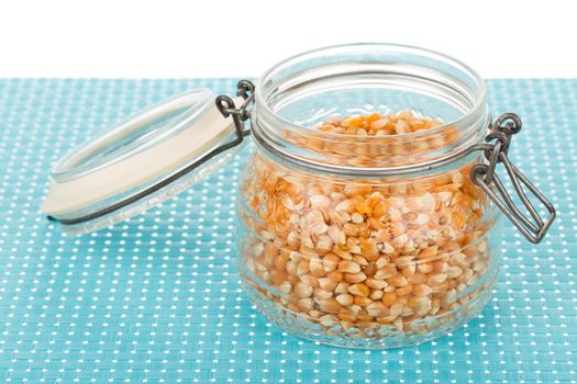 Corn seed in glass jar on blue tablemat.