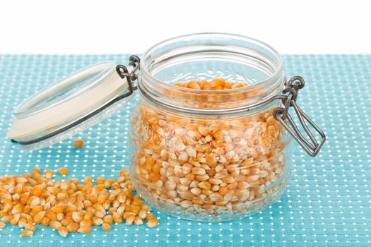 Corn seed in glass jar on blue tablemat.