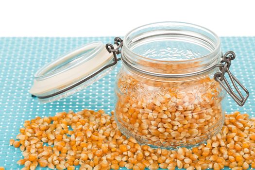 Corn seed in glass jar on blue tablemat.