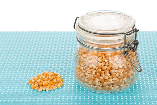 Corn seed in glass jar on blue tablemat.