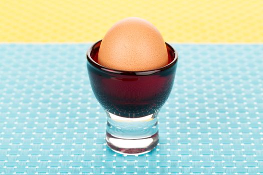 Single brown egg in eggcup on blue tablemat.