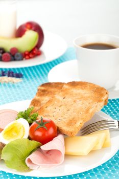 Breakfast with toast, cheese, sausage, ham, tomato, egg, cup of coffee and plate of fruits.