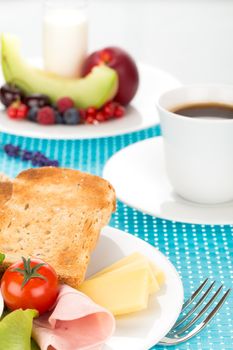 Breakfast with toast, cheese, sausage, ham, tomato, egg, cup of coffee and plate of fruits.