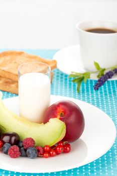 Healthy breakfast with a plate of fresh fruits, glass of milk and cup of coffee.