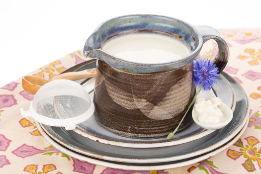 Kefir in argil jug with wooden spoon on rustic plate.