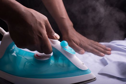 A person ironing a shirt with a steaming hot electric iron