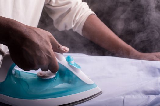 A person ironing a shirt with a steaming hot electric iron