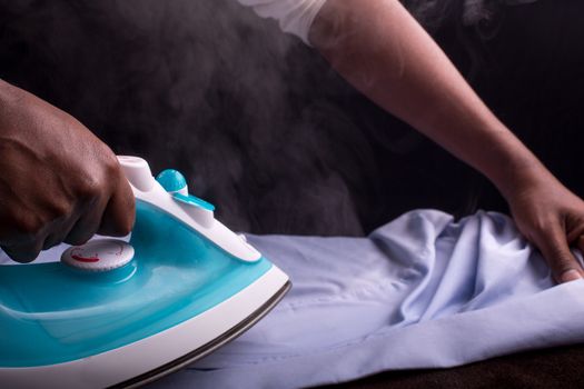 A person ironing a shirt with a steaming hot electric iron