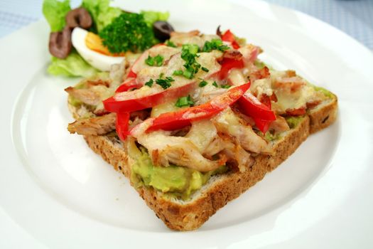 Grilled open chicken sandwich with avocado, peppers and cheese with a side salad.