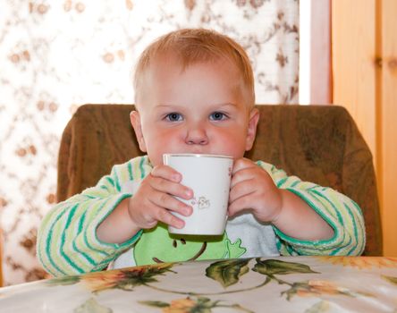 little boy is drinking at a table in the kitchen