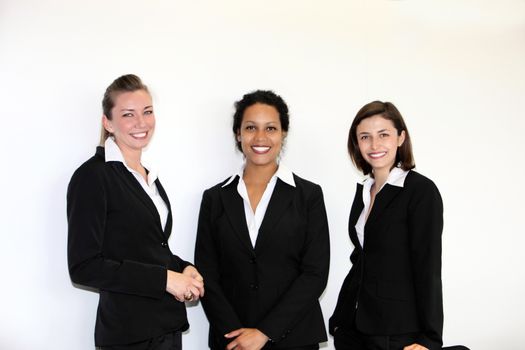 Three multiethnic attractive young businesswomen in stylish suits posing in a row smiling at the camera on white