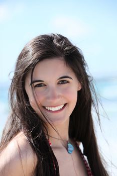 Beautiful young brunette woman with a beaming smile standing in the summer sun at the seaside, close up portrait