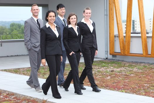 Stylish young business team of multiethnic men and women walking together along an outdoor cement pathway