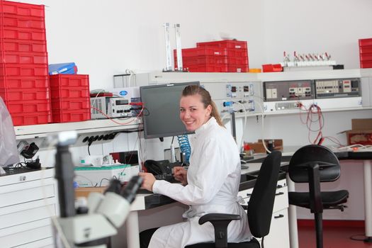 Confident female laboratory technician sitting at her desk in a modern chemical laboratory