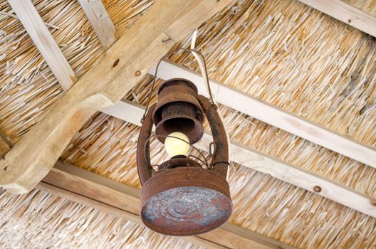 old rusty metal lamp hang on bower straw roof ceiling with electric bulb.