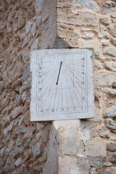 Old rectangular metal clock or sundial with hour graduations set into the corner of an old stone building