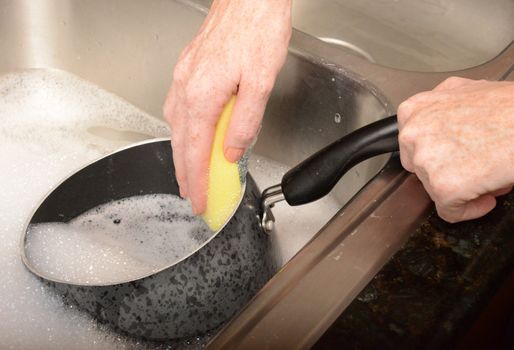 scrubbing pot with scour pad while washing dishes in soapy water