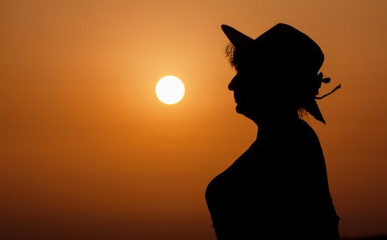 Silhouette woman portrait with hat against orange sunset