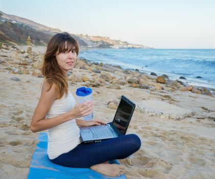 Young pretty woman with laptop on the beach by the ocean 