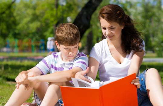 boy and a woman in a summer park reading a book together