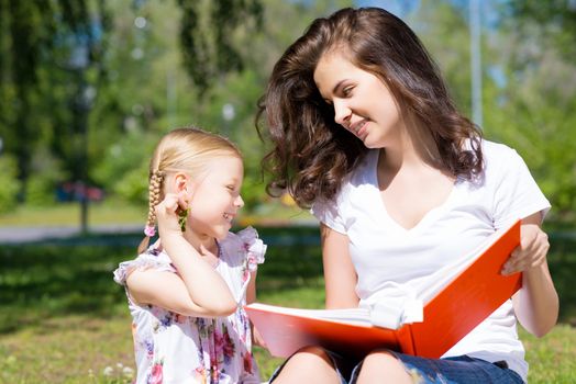 girl with the teacher reading a book together in the summer park