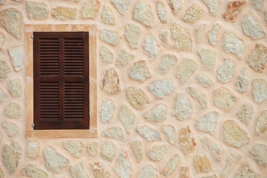 Window with closed wooden shutters in a natural stone wall of a house painted in a neutral colour with copyspace