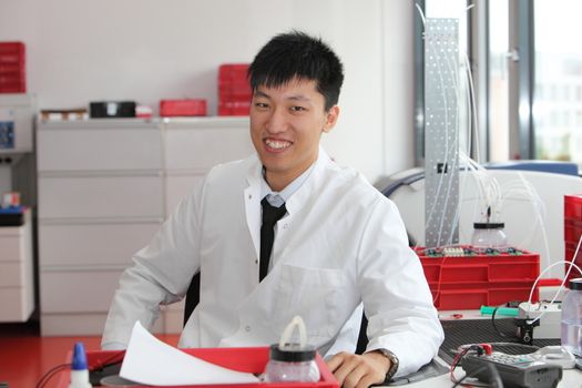 Smiling Asian laboratory technician sitting at his desk facing the camera in a modern laboratory