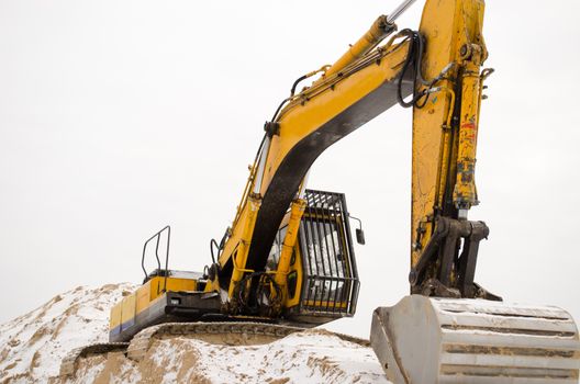 closeup of earthmover excavator stand on quarry pile sand pit soil earth covered with snow in winter.