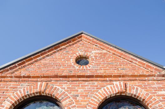 small round window and arch in retro architecture red brick building house roof on background of blue sky.