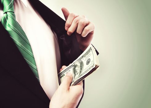 Business Man putting  a wad of cash in his suit jacket pocket on green vintage background