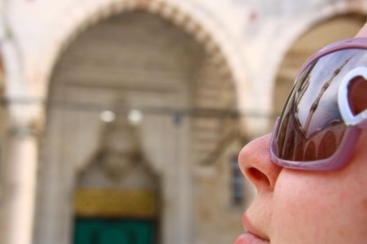 tourist girl in mosque looking minaret and reflection of minaret on sunglass