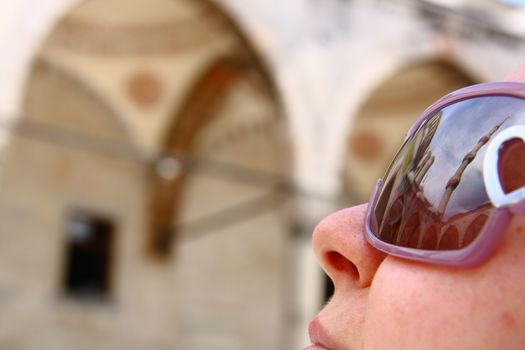 tourist girl in mosque looking minaret and reflection of minaret on sunglass