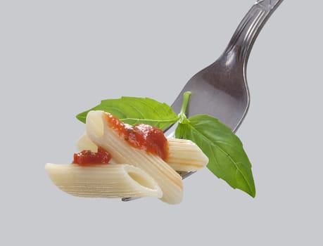 Some pasta with tomato sauce and green basil on the metal fork