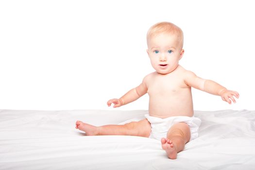 Cute happy smiling infant baby with blue eyes sitting on bed, on white.