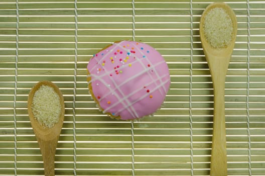 top view pink cupcake with colorful sprinkles and spoon of sugar on wooden background