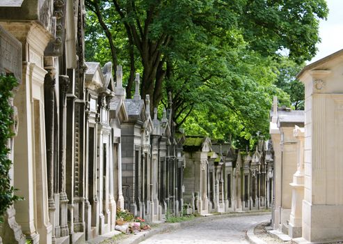 Aged and weathered mausoleums lining both sides of a path in Pere Lachaise Cemetery, Paris, France