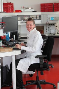 Confident attractive young female lab technician sitting at her work station in a modern chemical laboratory