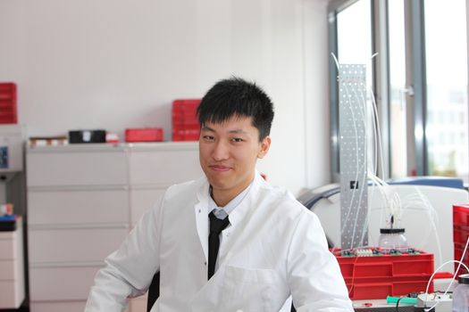 Young male Asian technician working in a laboratory sitting in his white lab coat smiling at the camera